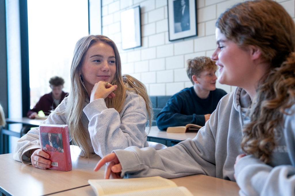 Twee leerlingen die aan een lestafeltje in de klas met elkaar over boeken praten. 